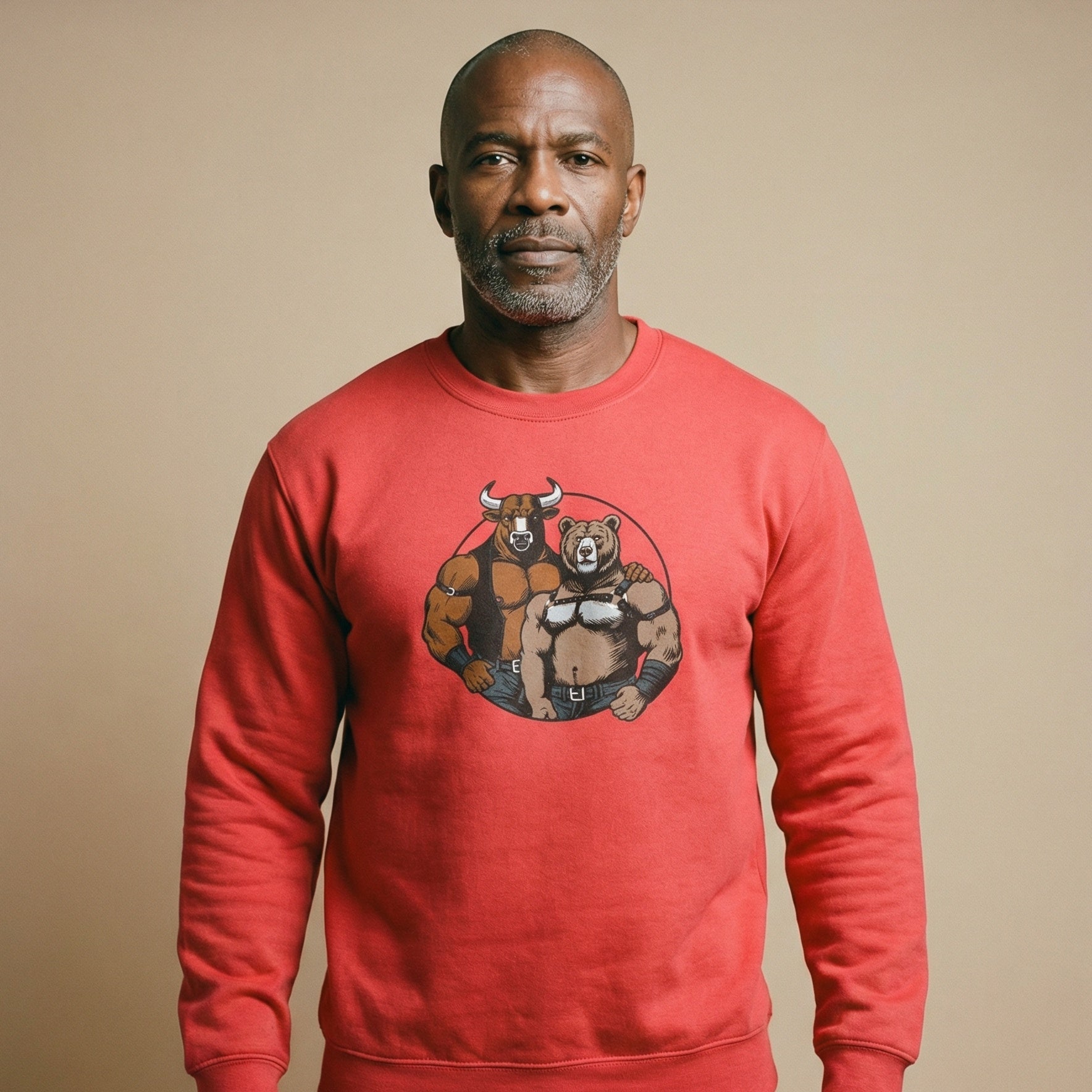 A studio portrait of a middle-aged Black man with a salt-and-pepper beard and shaved head, looking directly at the camera. He is wearing a bright red sweatshirt featuring a circular graphic of a muscular bull and bear in leather attire. The background is a solid, neutral beige, and a portion of his legs in black underwear is visible below the sweatshirt. #color_Red