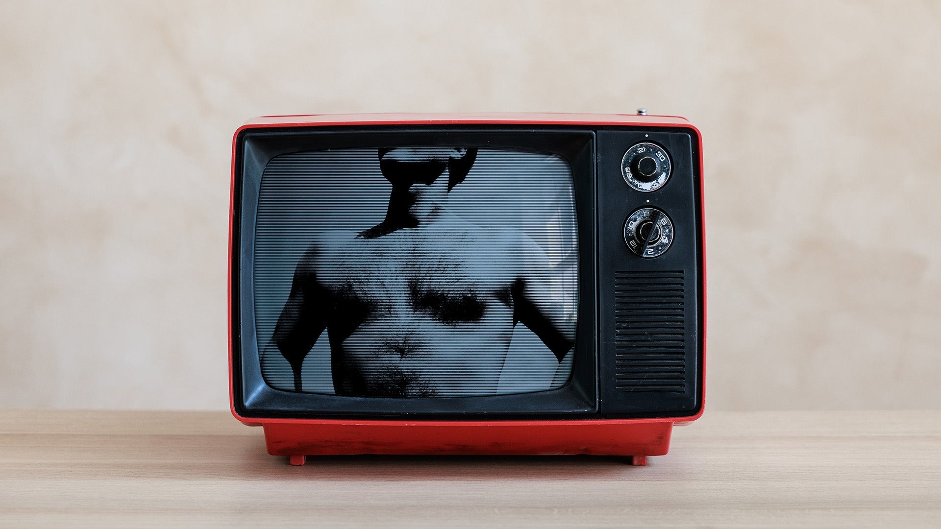 A vintage red television on a wood surface, its screen showing a high-contrast halftone image of a shirtless man's hairy chest, his head cropped above the frame.