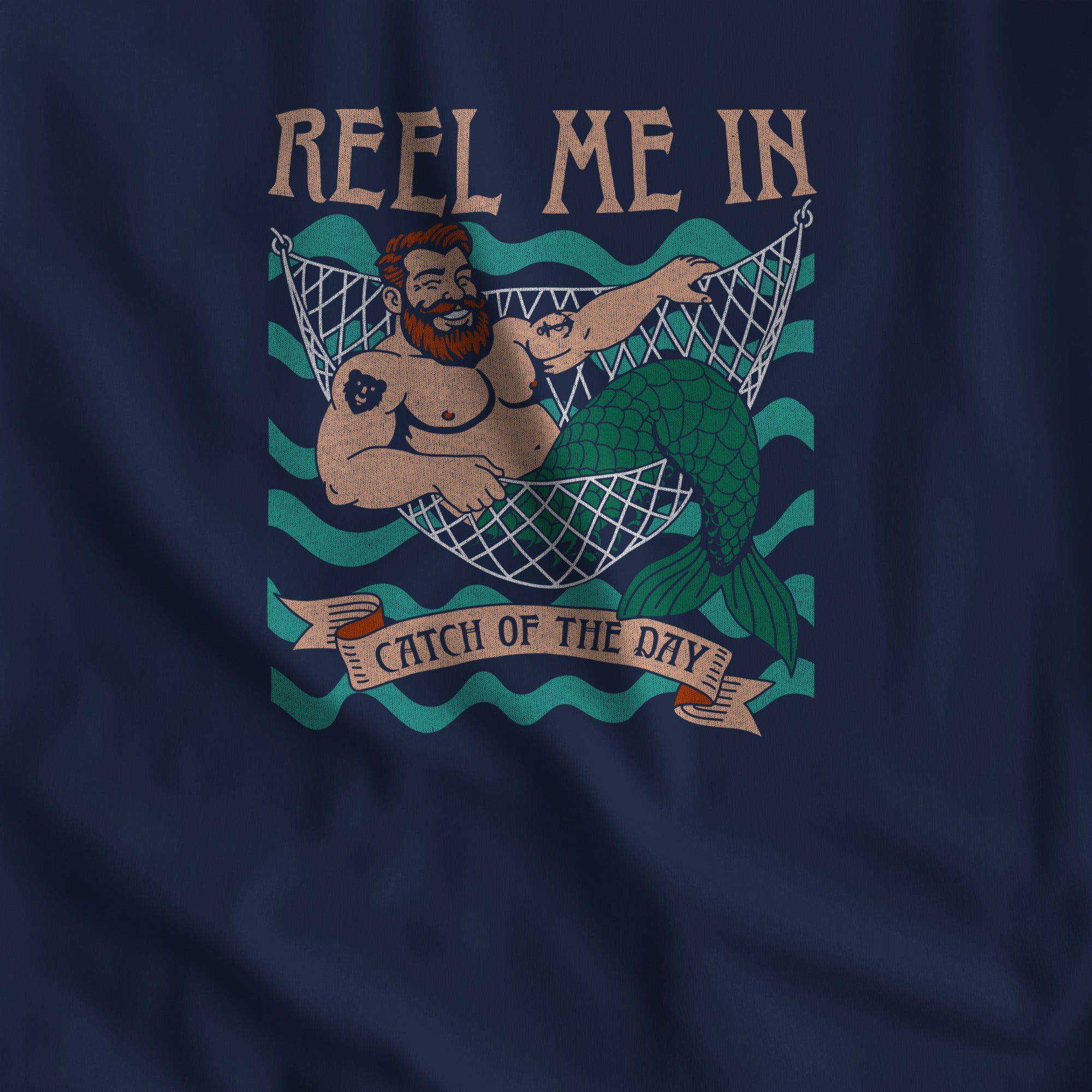 Close-up of the Reel Me In merman print with Catch of the Day banner on a navy tank. #color_Navy