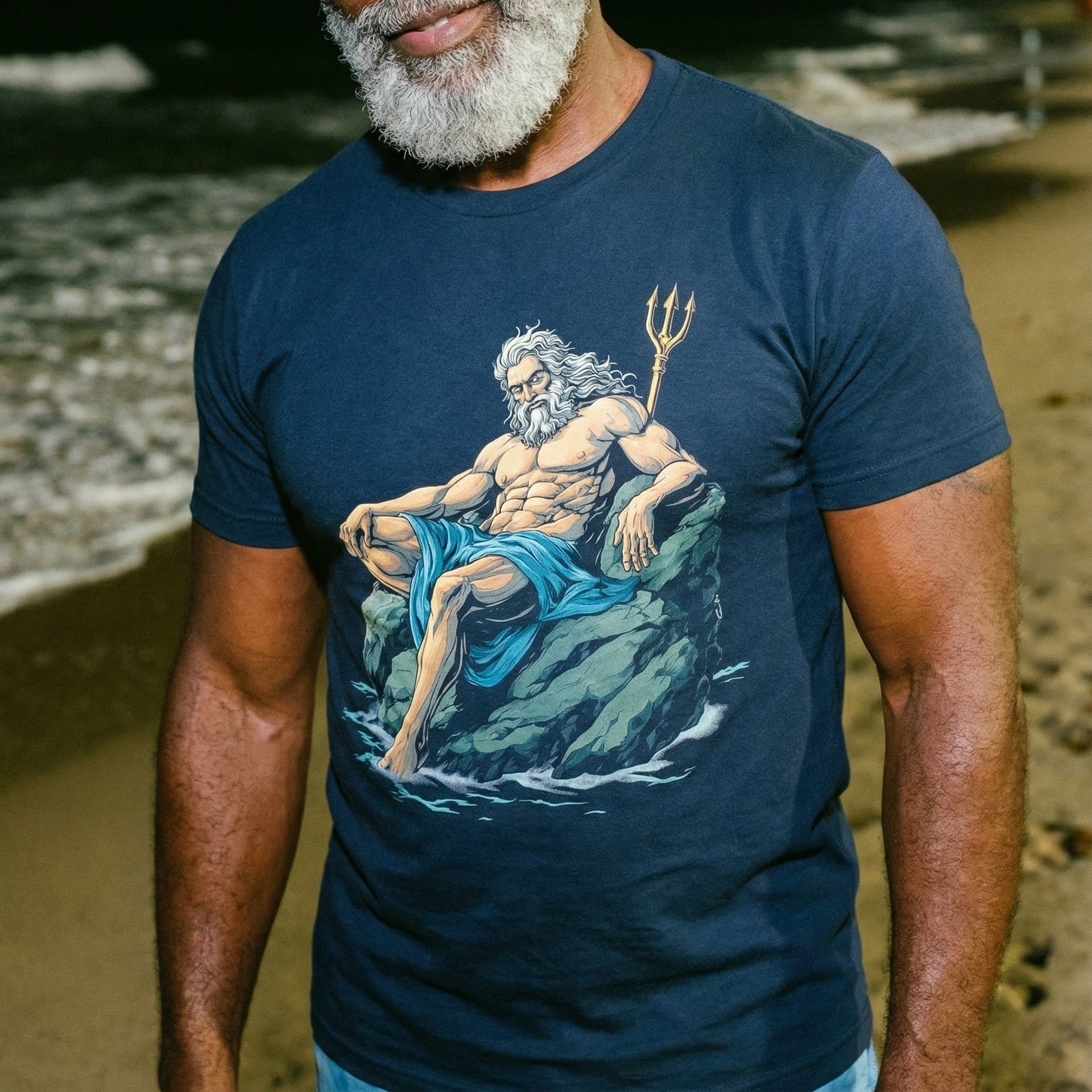 A close-up image of a man with a well-groomed grey beard wearing a dark blue t-shirt. The shirt features a large graphic illustration of Poseidon, depicted as a muscular man with white hair and beard, sitting on a rock in the ocean and holding a golden trident. The background shows a dimly lit beach scene at night with waves breaking on the shore. #color_Navy